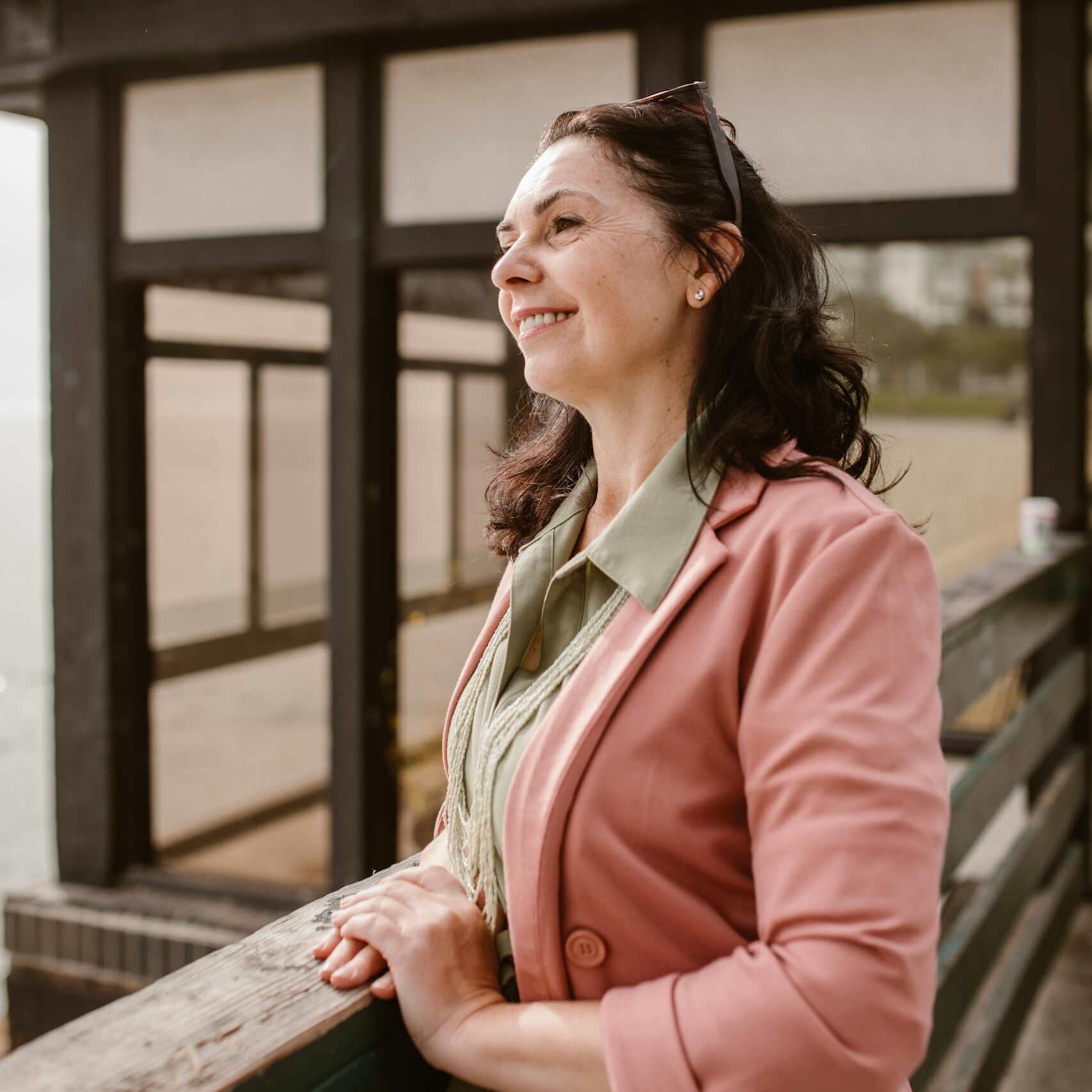Caucasian woman standing outdoors in a pink blazer, smiling and enjoying the view.